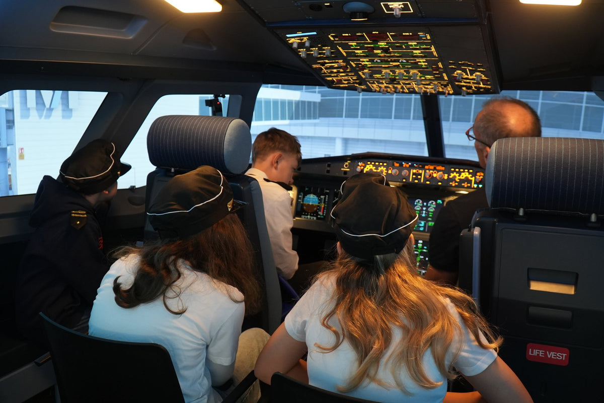 Geburtstagsgäste mit Pilotenmützen schauen ins Cockpit des A320 Flugsimulators