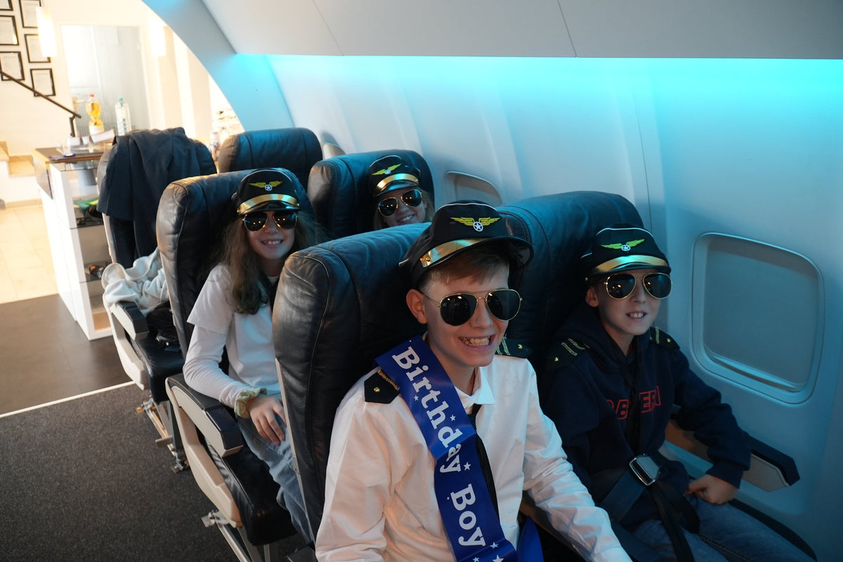 Geburtstagskind mit Schärpe und Freunde mit Pilotenmützen in der Kabine des A320 Flugsimulators
